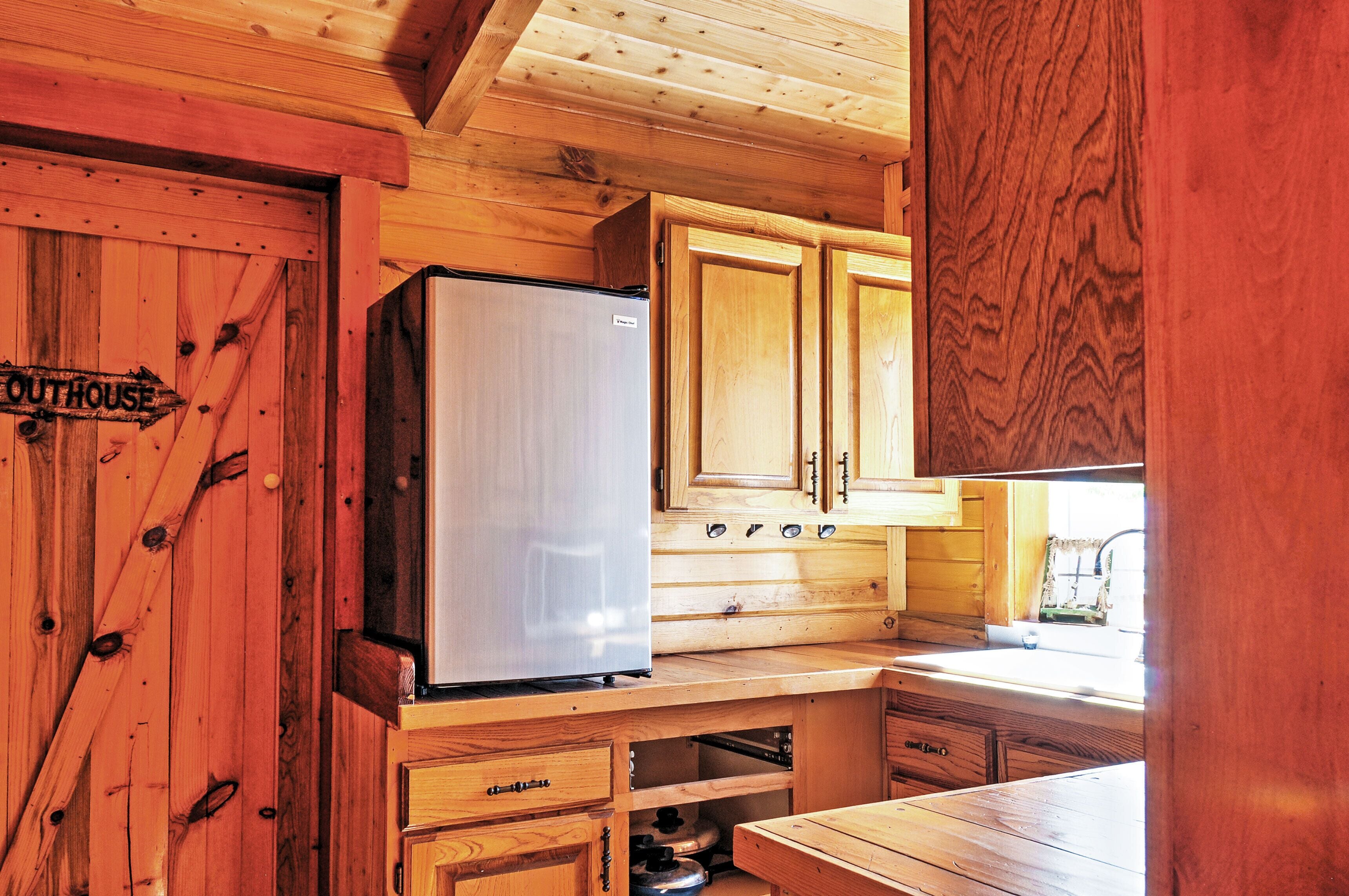Interior de una cabaña de madera con refrigerador, armarios de madera y un lavamanos.