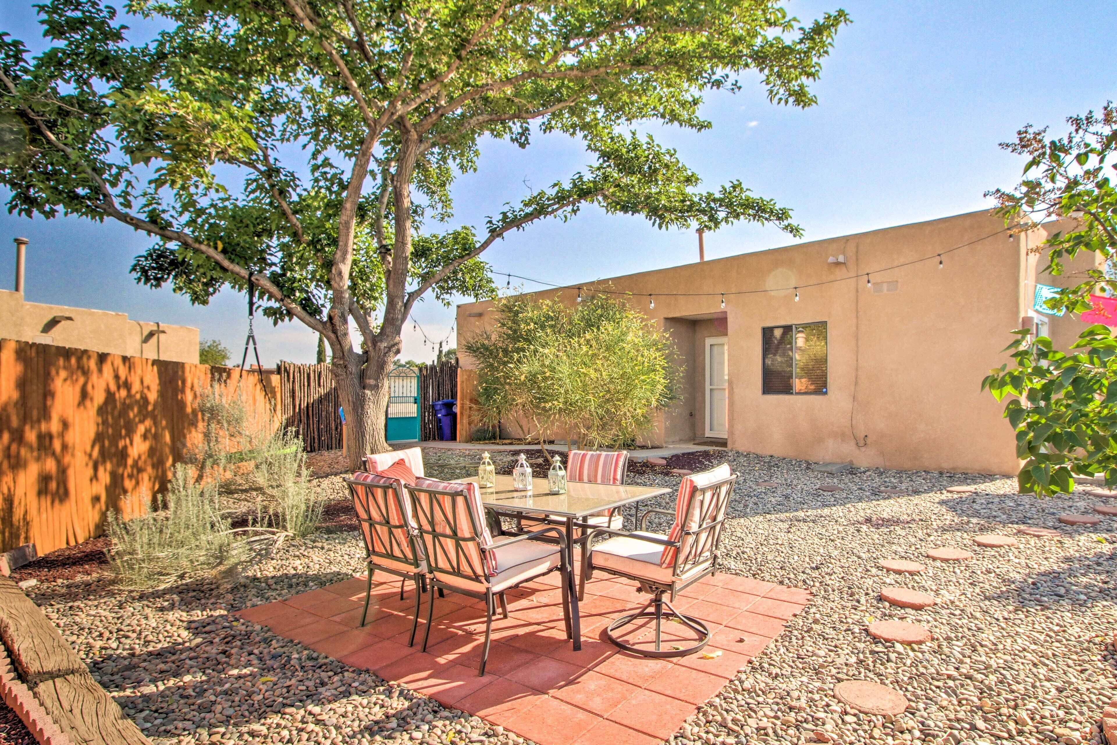 A patio with a table and chairs, surrounded by a gravel area and a wooden fence.