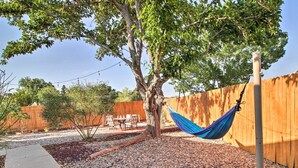 A tree with a hammock tied to it, a wooden fence, and a patio area with a table and chairs. - Mountain-view Albuquerque Townhome w/ Patio! (Albuquerque)