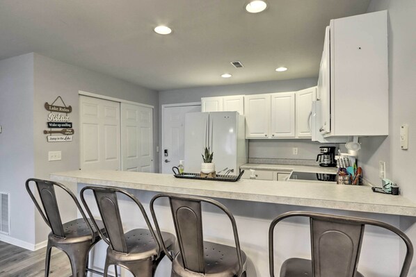 A modern kitchen with white cabinets, a stainless steel refrigerator, and a bar area with three chairs.
