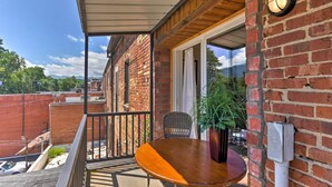 A balcony with a wooden table and chair, a potted plant, and a brick wall. - Modern Main St. Apt in Downtown Waynesville! (Waynesville)