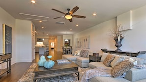 A spacious living room with a large sofa, a coffee table, and a ceiling fan. There is a dining area in the background with a chandelier. - Modern Main St. Apt in Downtown Waynesville! (Waynesville)