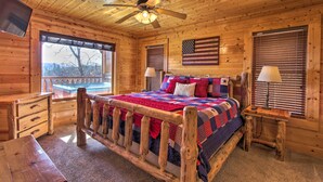 Un dormitorio de cabaña de madera con cama, escritorio, silla, ventilador de techo y ventana con persianas.