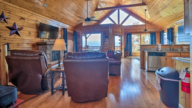 Una cabaña amplia con interior de madera, chimenea, asientos de cuero, televisor y zona de cocina.
