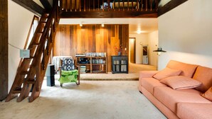 A cozy living room with a staircase, wooden walls, a sofa, a chair, and a bookshelf. - Peaceful Applegate River Valley Sanctuary! (Grants Pass)