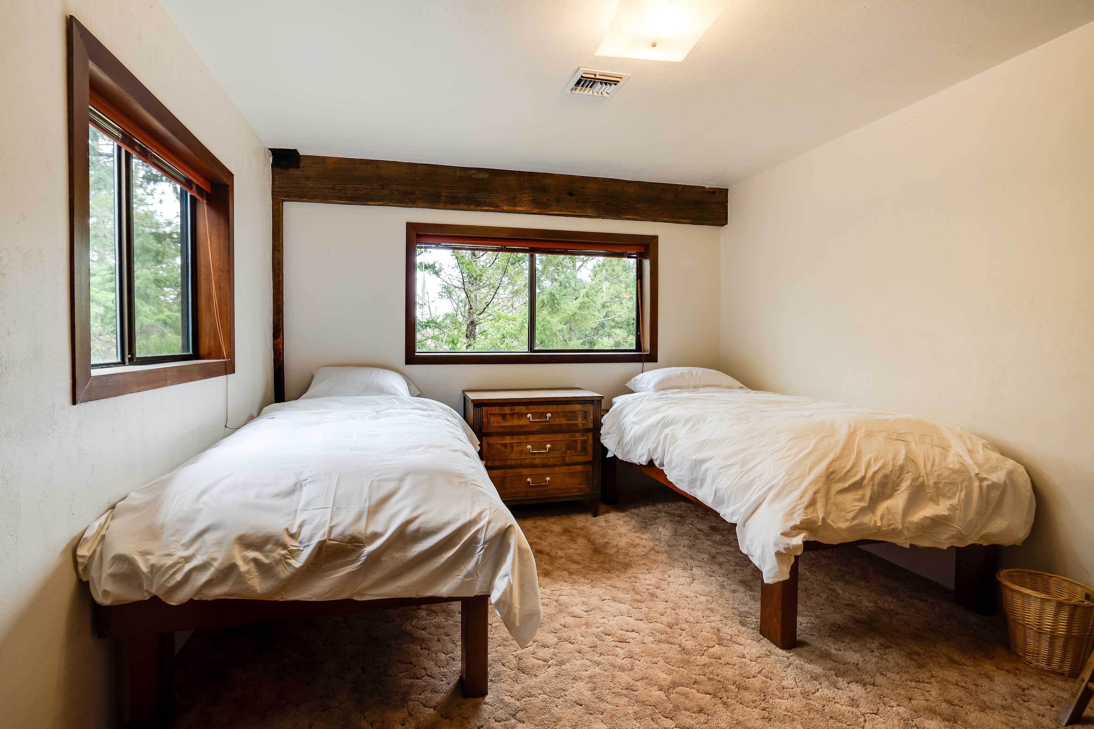 Un dormitorio con dos camas, una mesita de noche de madera, una ventana y una rejilla en el techo.