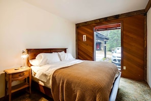 A bedroom with a wooden headboard, a bedside table with a lamp, a bed with white linens, and a view of a car through a window. - Peaceful Applegate River Valley Sanctuary! (Grants Pass)
