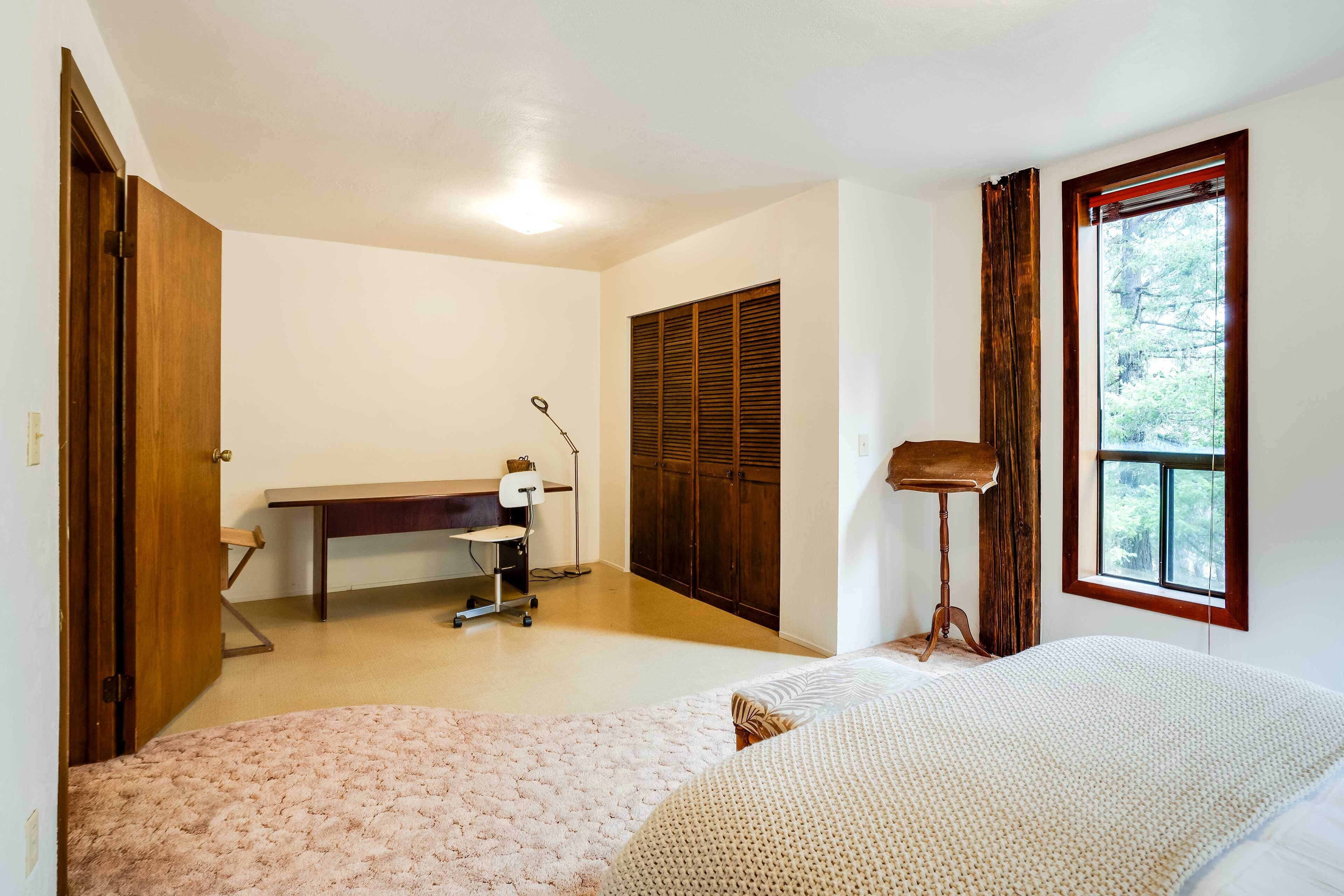 A bedroom with a bed, a desk, a chair, a wardrobe, and a window.