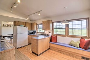A modern kitchen with wooden cabinets, a built-in island, and a seating area with cushions. - Montana Cottage: Easy Drive to Glacier Natl Park! (Columbia Falls)
