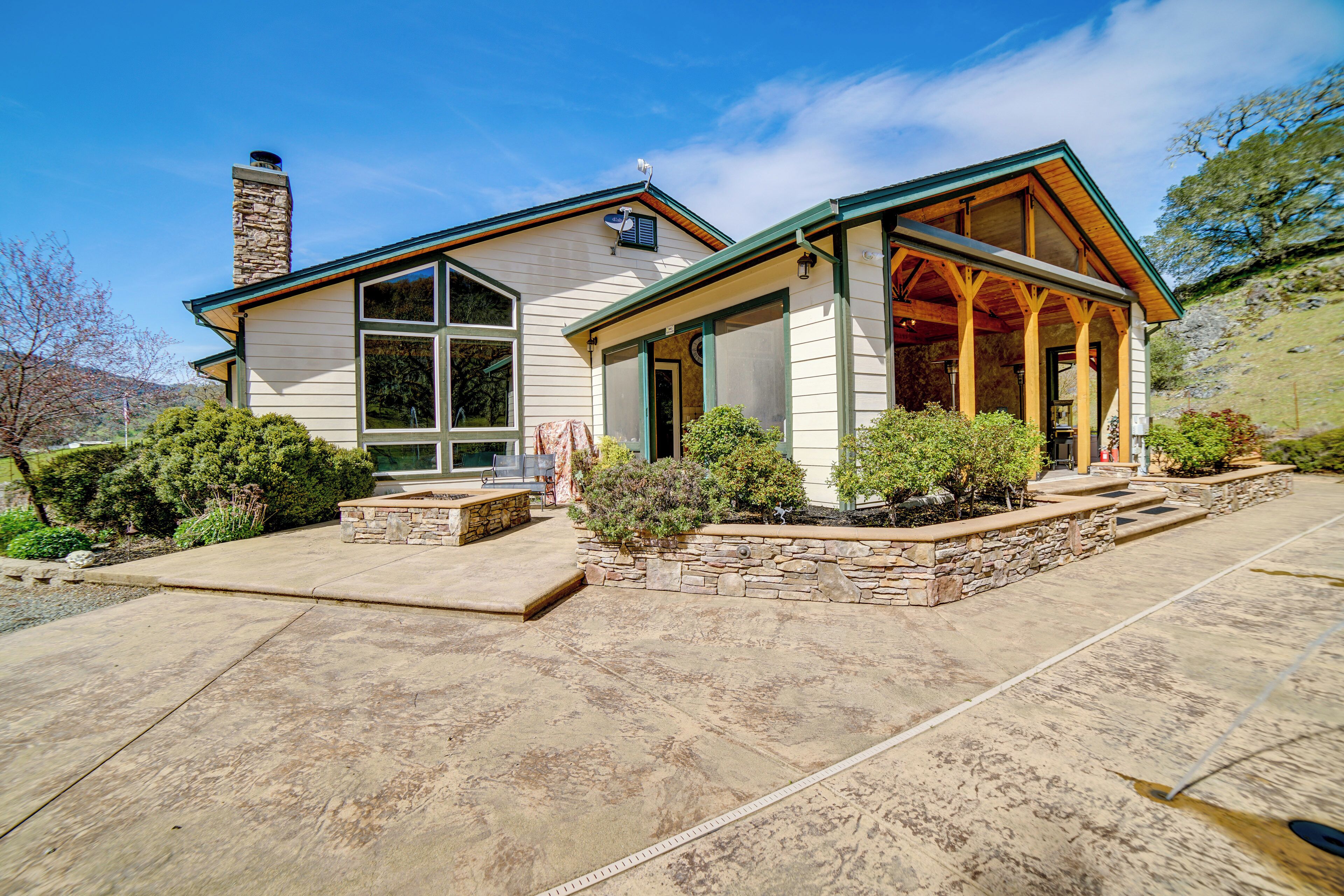 A two-story house with a stone chimney, a covered porch, and a stone retaining wall.