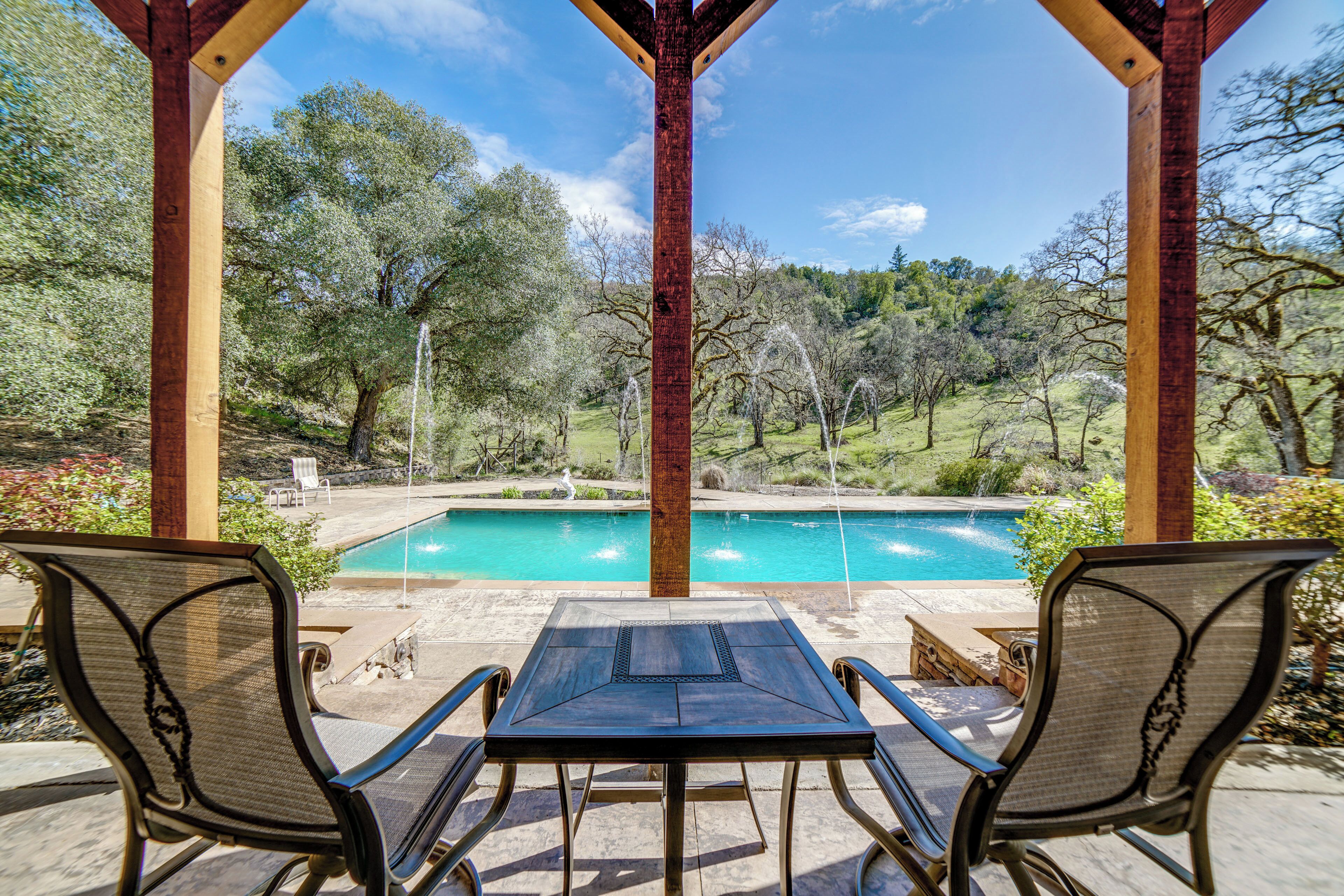 A covered patio with two chairs and a table overlooking a swimming pool.