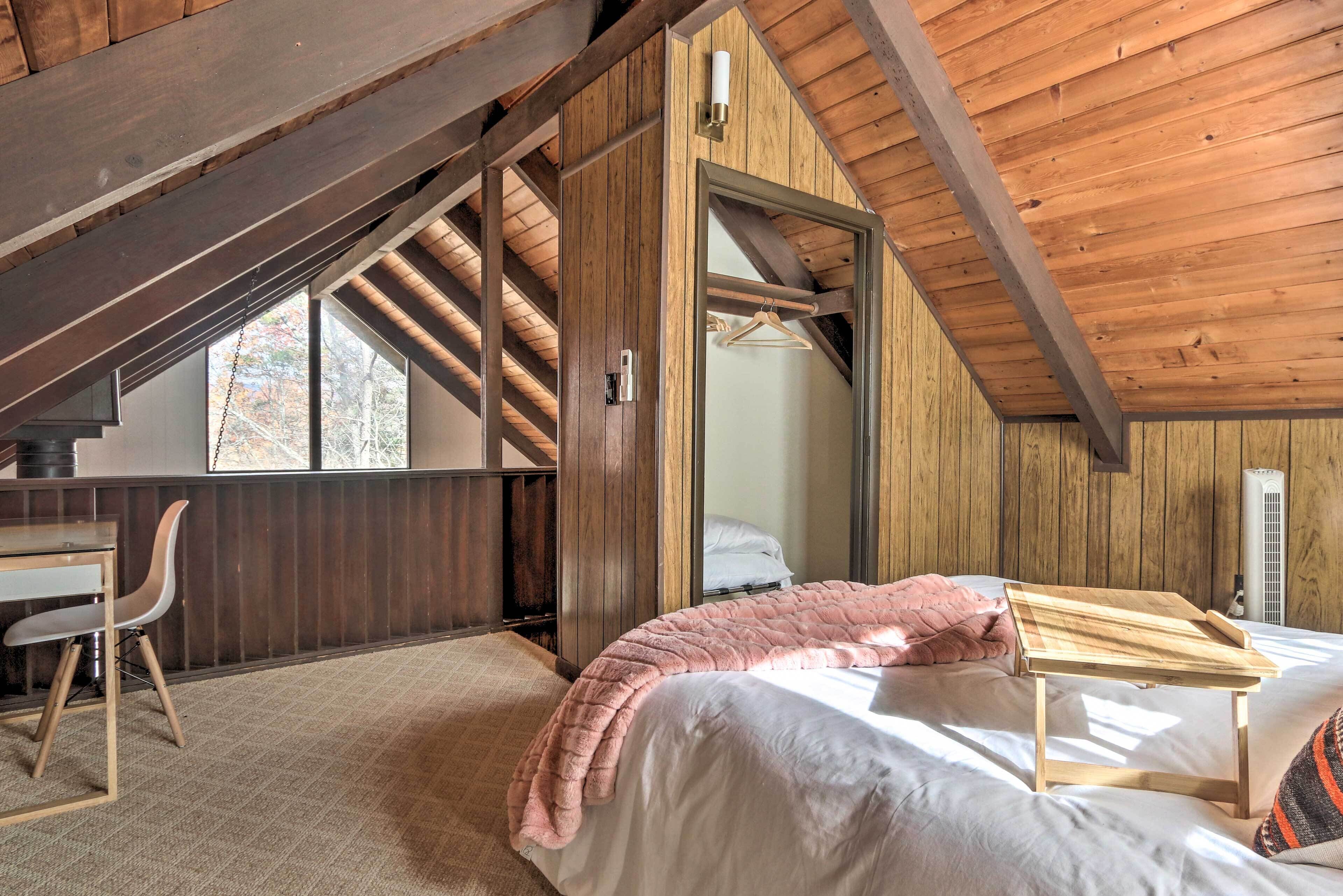 A bedroom with a bed, a desk, and a chair. There is a window with a view of trees.
