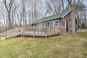 A cabin with a stone chimney, wooden deck, and a view of the surrounding forest. - Pickerel Lake Retreat w/ Grill, 15 Mi to Ski! (Petoskey)