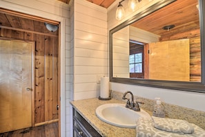 A bathroom with a wooden door, a white sink, a mirror, and a towel. - Pickerel Lake Retreat w/ Grill, 15 Mi to Ski! (Petoskey)