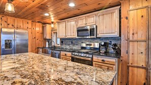 Cucina con mobili in legno, elettrodomestici in acciaio inossidabile, piani di lavoro in granito e schienale in pietra.