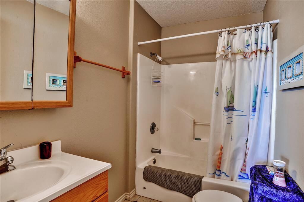A bathroom with a white sink, wooden vanity, a shower with a white curtain, and a mirror with a wooden frame.