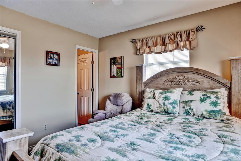 A bedroom with a bed, a chair, a window with curtains, and a door.
