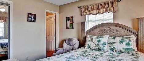 A bedroom with a bed, a chair, a window with curtains, and a door.