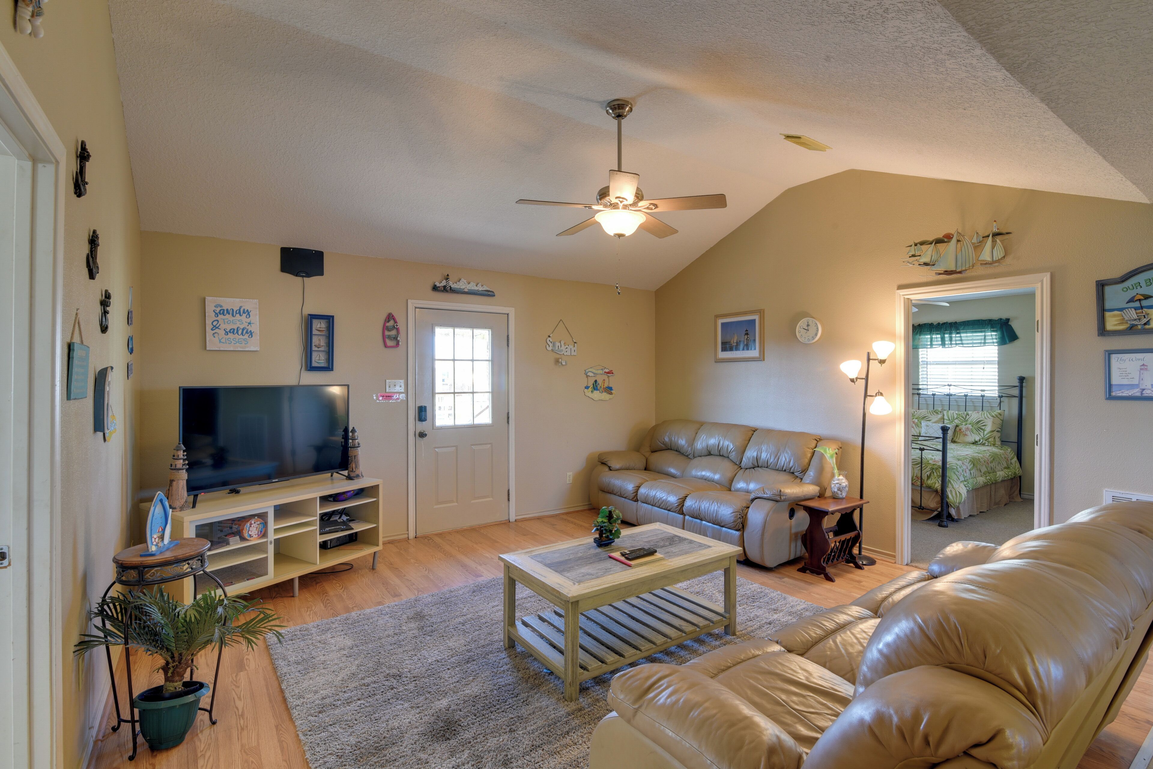 A living room with a television, leather sofa, coffee table, and a ceiling fan.
