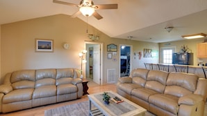 A spacious living room with two beige leather sofas, a coffee table, and a ceiling fan. - Walk to Shore & Restaurants: Surfside Beach Home! (Freeport)
