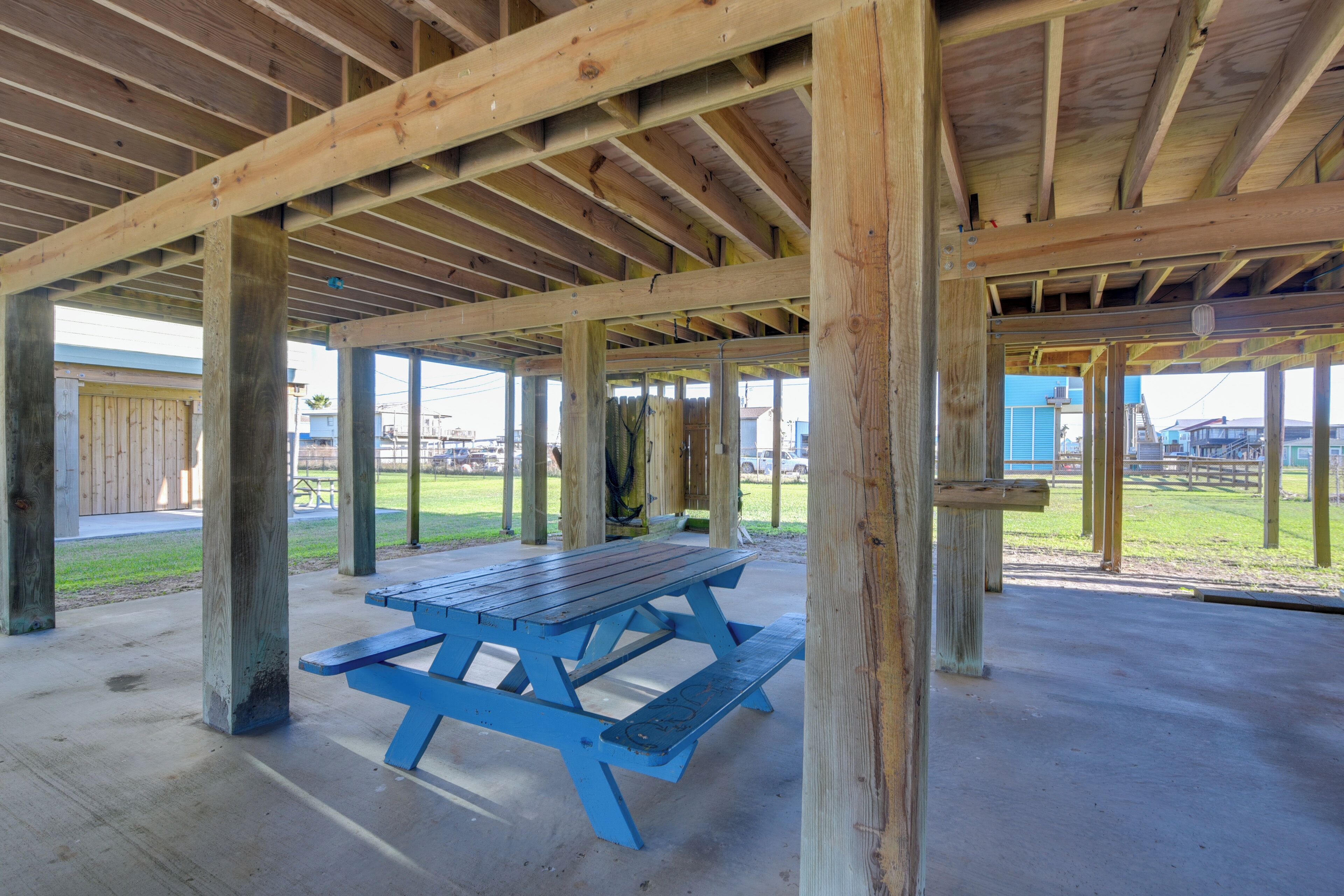 A covered picnic area with a blue picnic table, wooden beams, and a concrete floor.