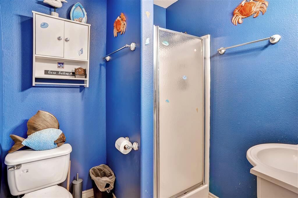 Une salle de bain avec un mur bleu, des toilettes blanches, une douche avec une porte en verre et un lavabo.
