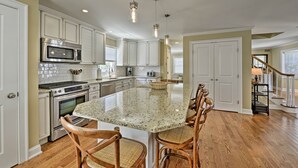 Una cocina amplia con armarios blancos, una isla grande con taburetes de bar, electrodomésticos de acero inoxidable e iluminación colgante.