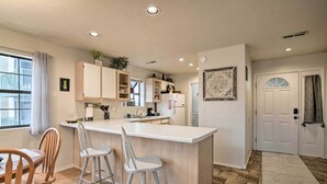 A modern kitchen with a central island, bar stools, wooden chairs, and a dining table.
