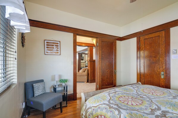 Un dormitorio con cama, una silla, una mesita de noche y una puerta que da a otra habitación.