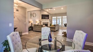 A modern living room with a glass coffee table, white upholstered chairs, a fireplace, and a television mounted above it. - Bright Hopkins Home w/ Game Room & Fire Pit! (Hopkins)