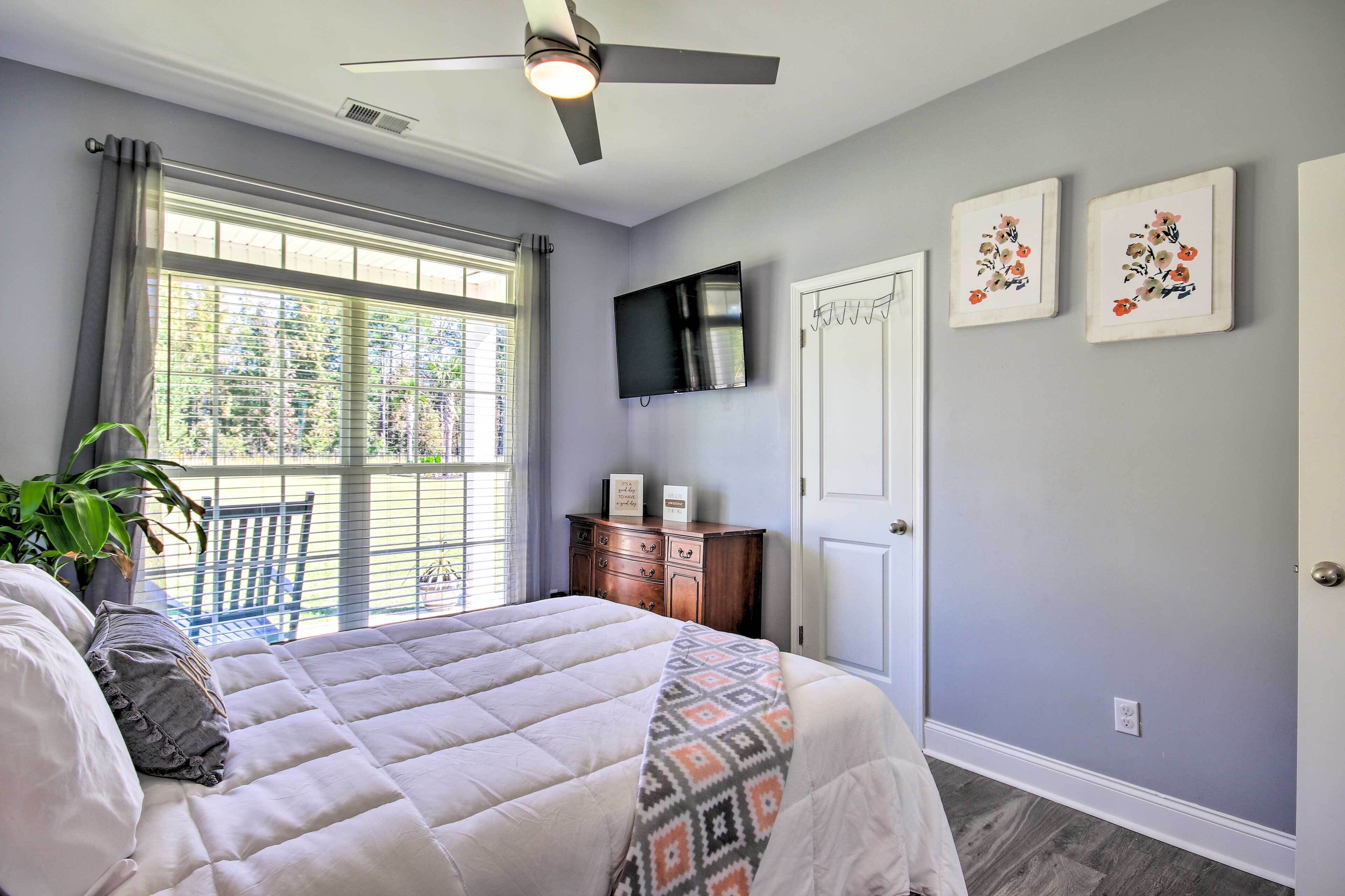 A bedroom with a bed, a ceiling fan, a TV, a dresser, and a window with curtains.