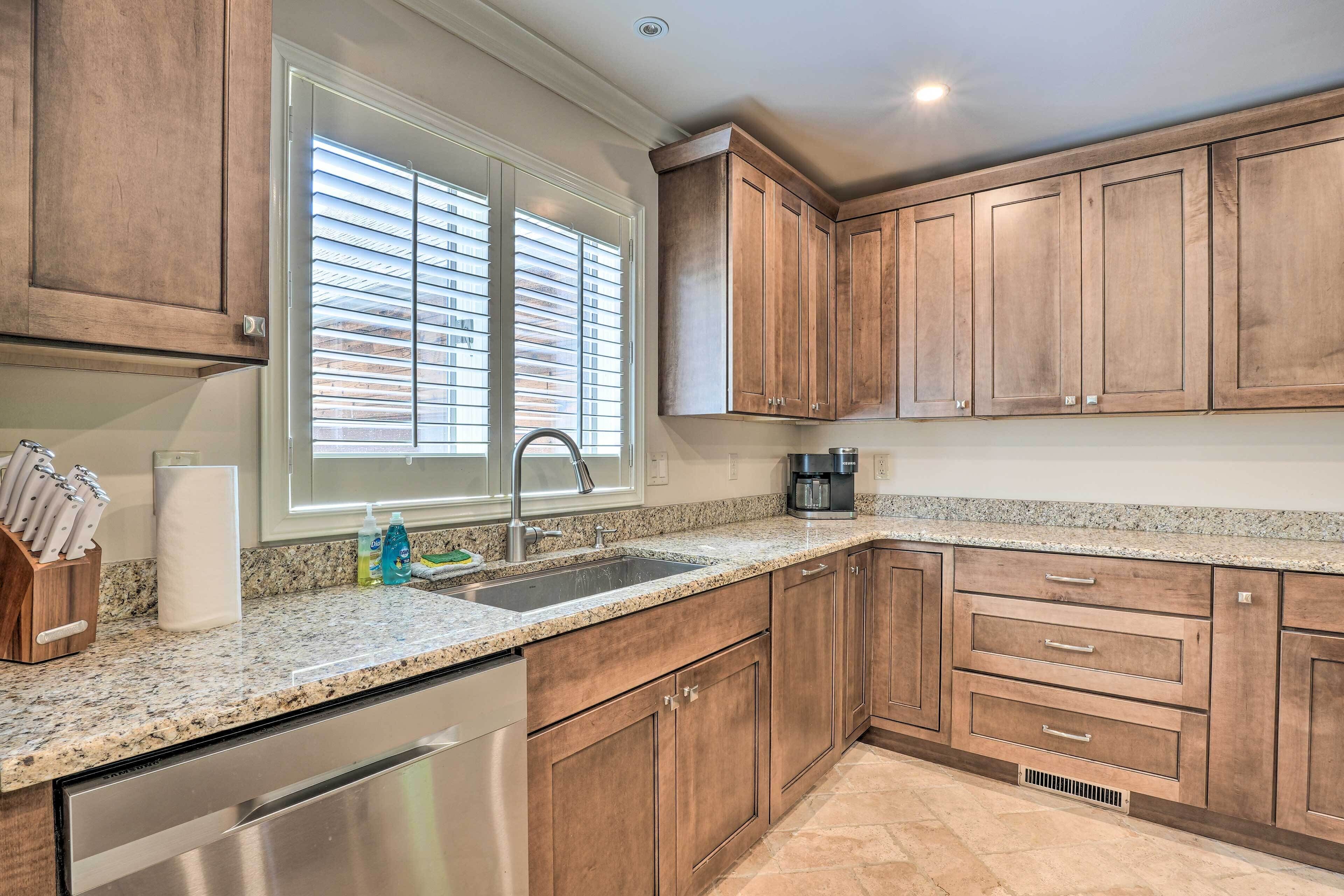 A kitchen with wooden cabinets, a granite countertop, stainless steel appliances, and a window with blinds.