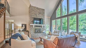 A spacious living room with a stone fireplace, large windows, and a comfortable seating area. - Spacious Lakefront Home w/ Private Dock! (Hollister)