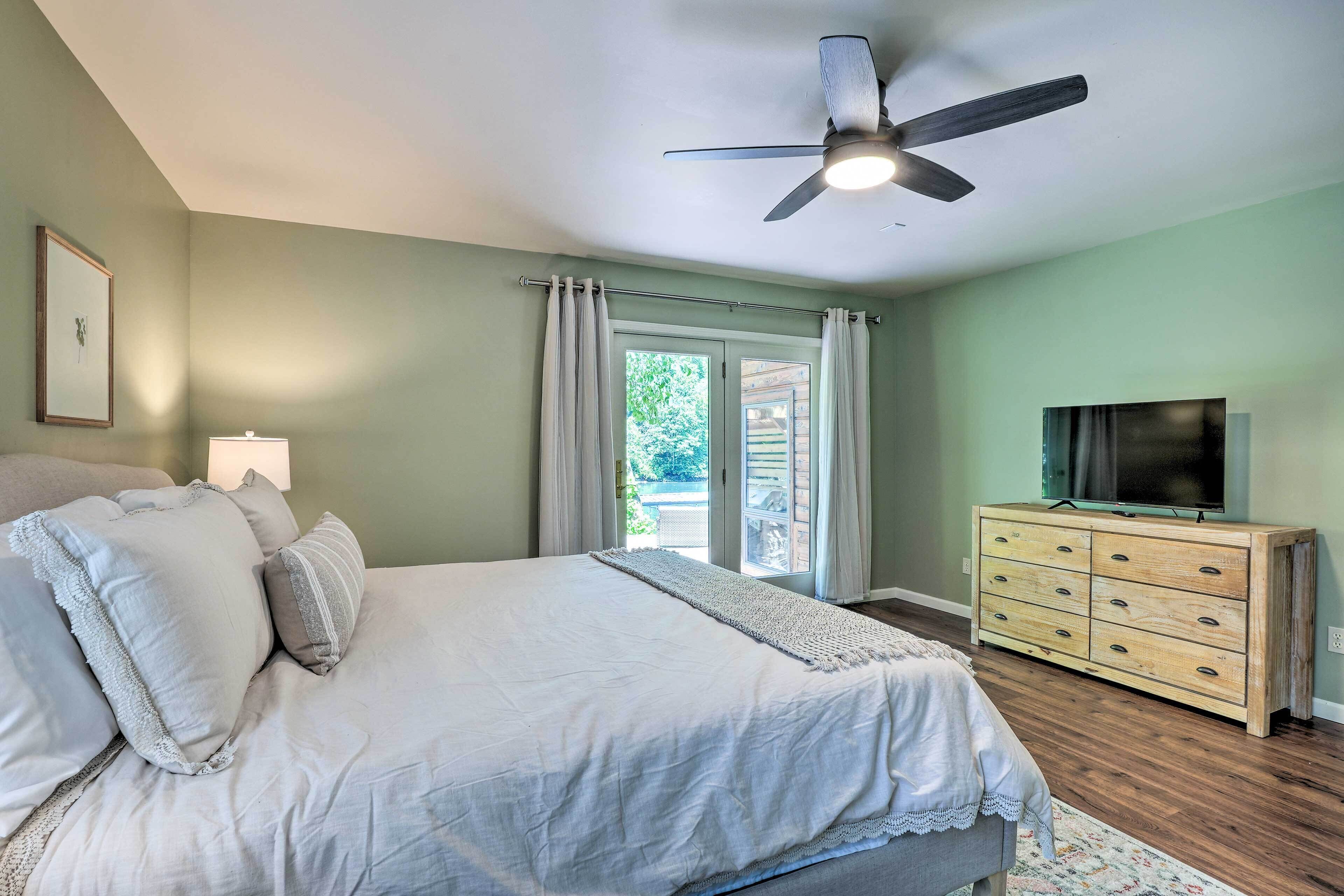 A bedroom with a bed, a dresser, a ceiling fan, and a television.