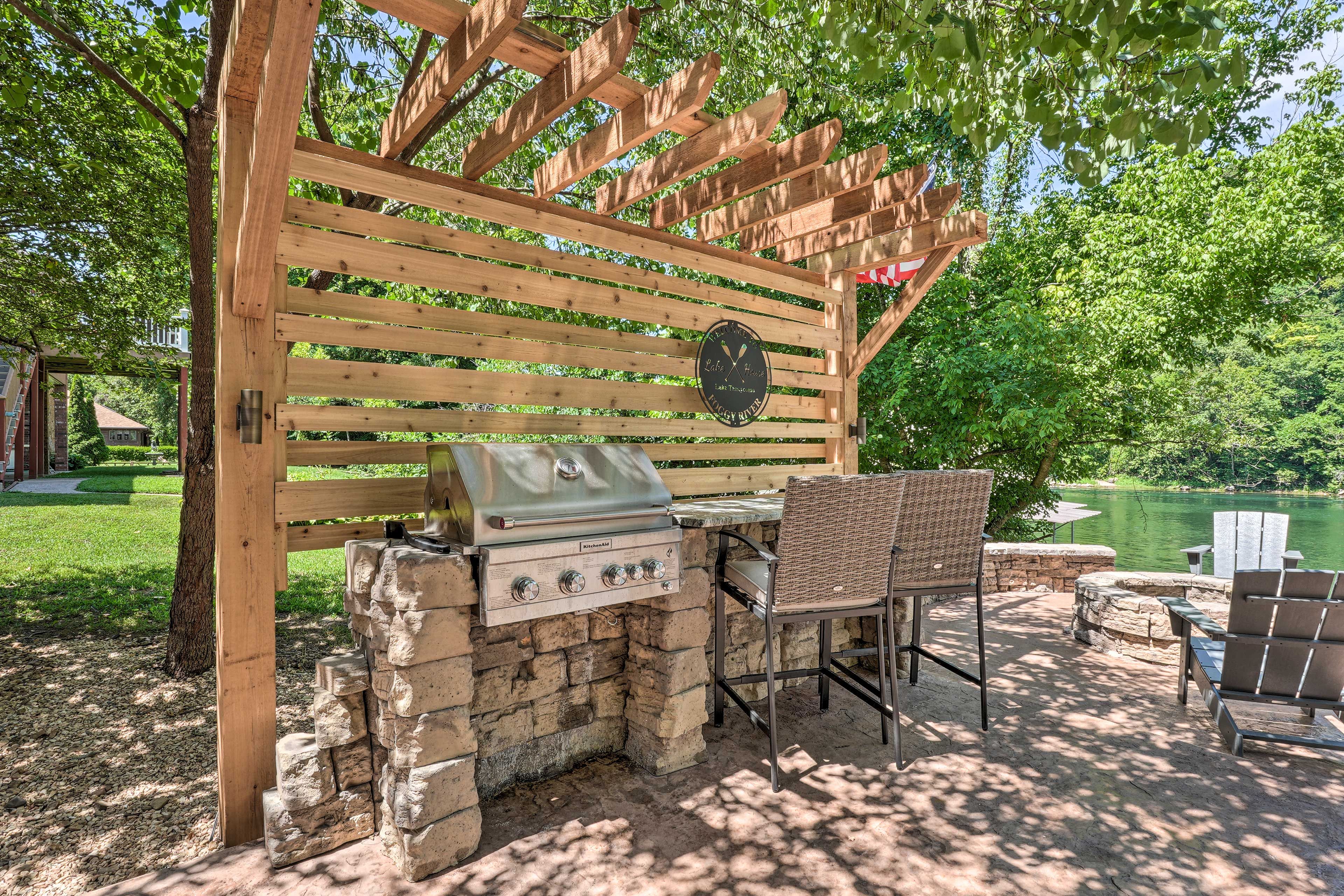 An outdoor grill area with a stone-built grill, a wooden pergola, and wicker chairs.