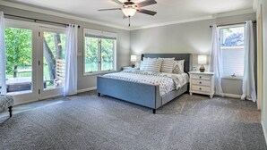 A bedroom with a bed, nightstands, a ceiling fan, and large windows. - Spacious Lakefront Home w/ Private Dock! (Hollister)
