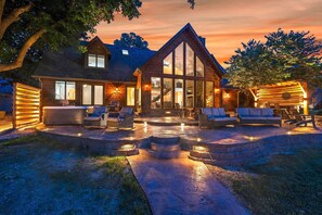A large, two-story log cabin with a spacious patio area featuring outdoor seating and a fire pit. - Spacious Lakefront Home w/ Private Dock! (Hollister)