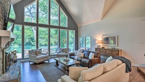 A spacious living room with large windows, a fireplace, and a view of a lake. - Spacious Lakefront Home w/ Private Dock! (Hollister)