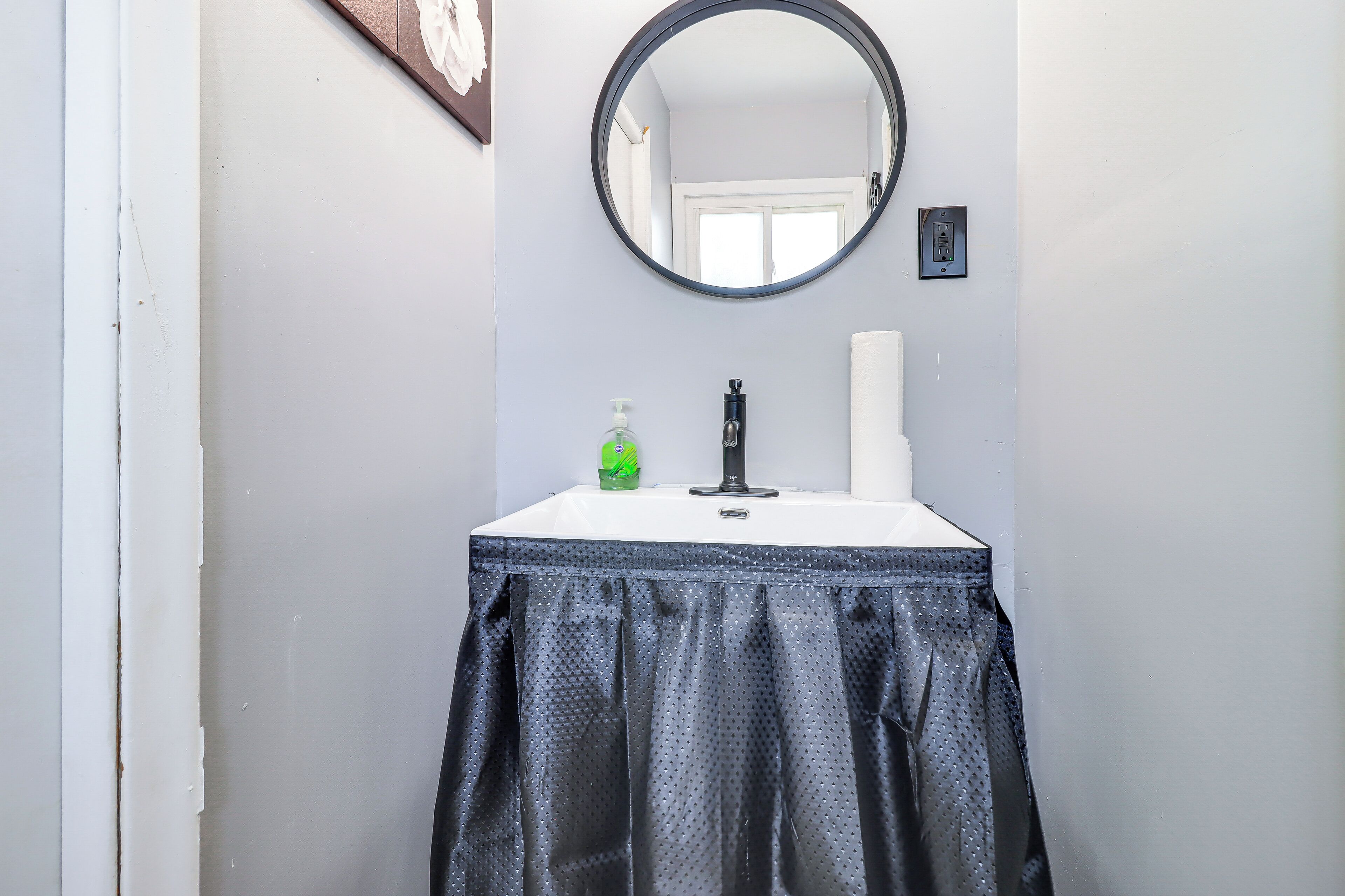 A bathroom with a white sink, a black faucet, a green soap dispenser, and a white towel.