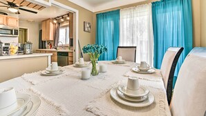 A dining area with a table set for four, a kitchen in the background, and blue curtains on the windows. - Detroit Home w/ Pool & Yard, 15 Mi to Downtown! (Redford)