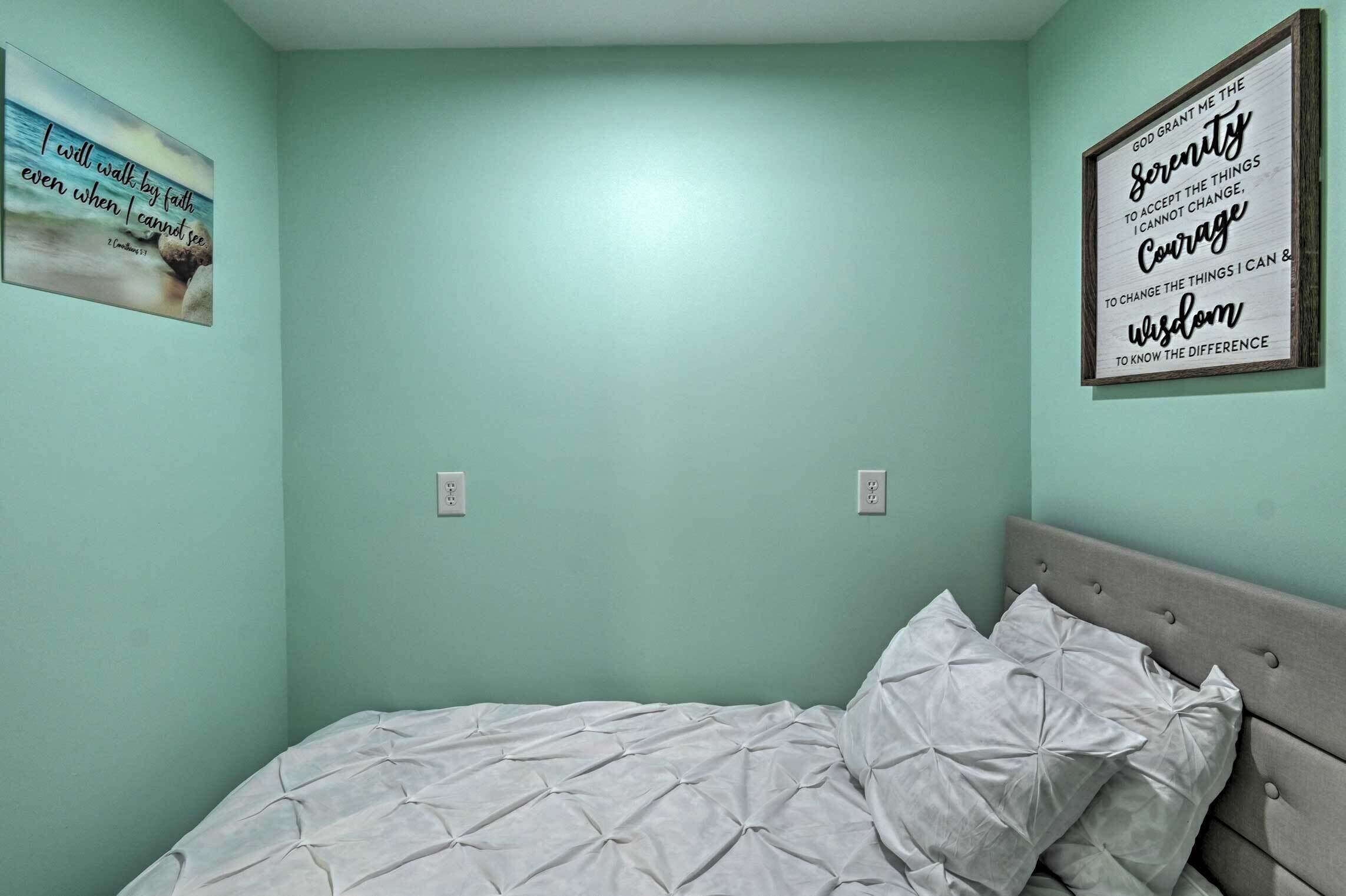 A bedroom with a bed, a wall with a framed inspirational quote, and a small picture on the wall.