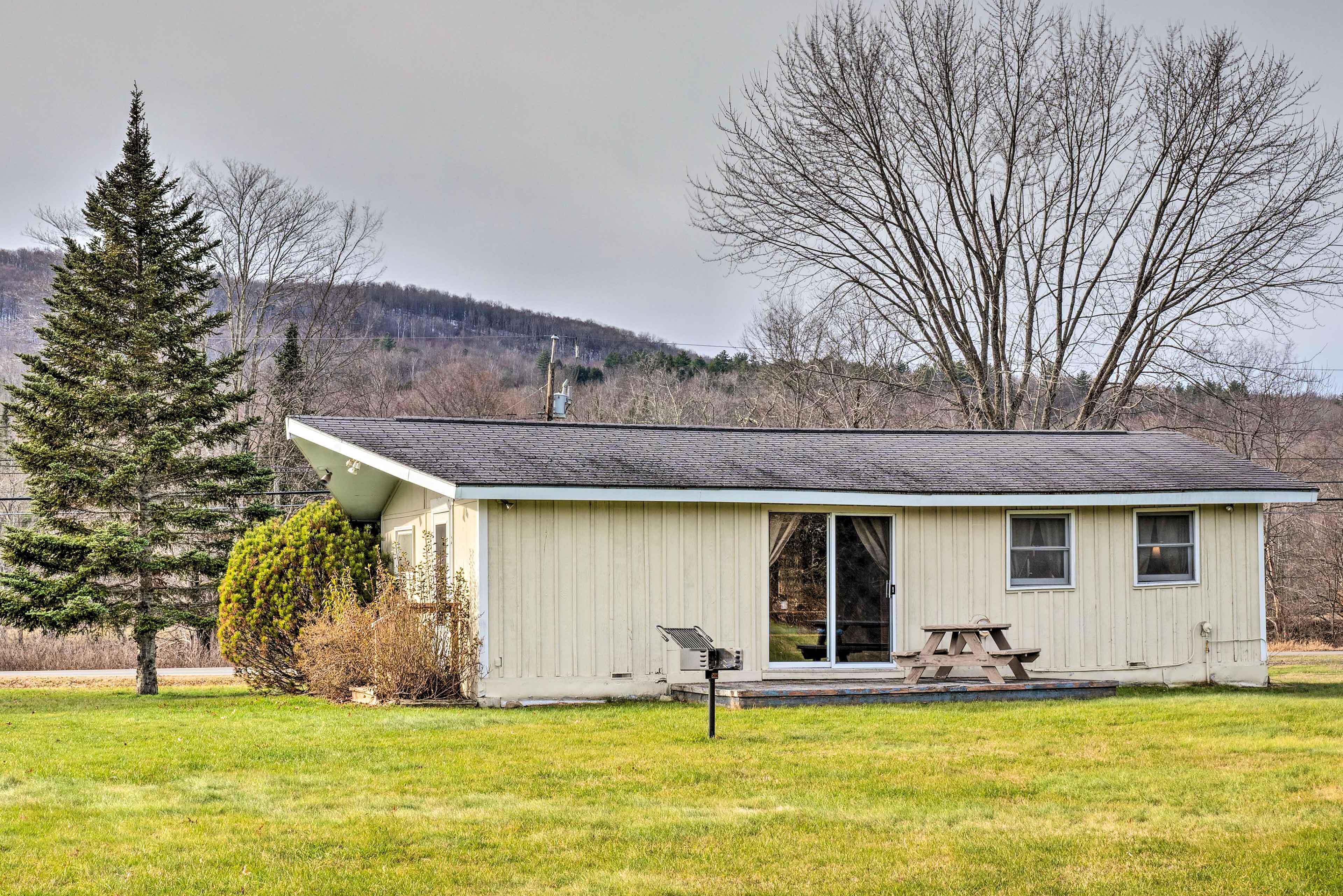A small, single-story cabin with a sloped roof, a front door, and a small porch area with a picnic table.