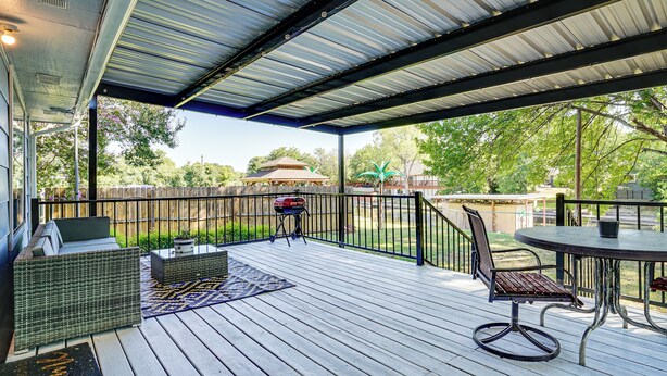 A covered outdoor patio with a wooden deck, wicker furniture, and a barbecue grill.