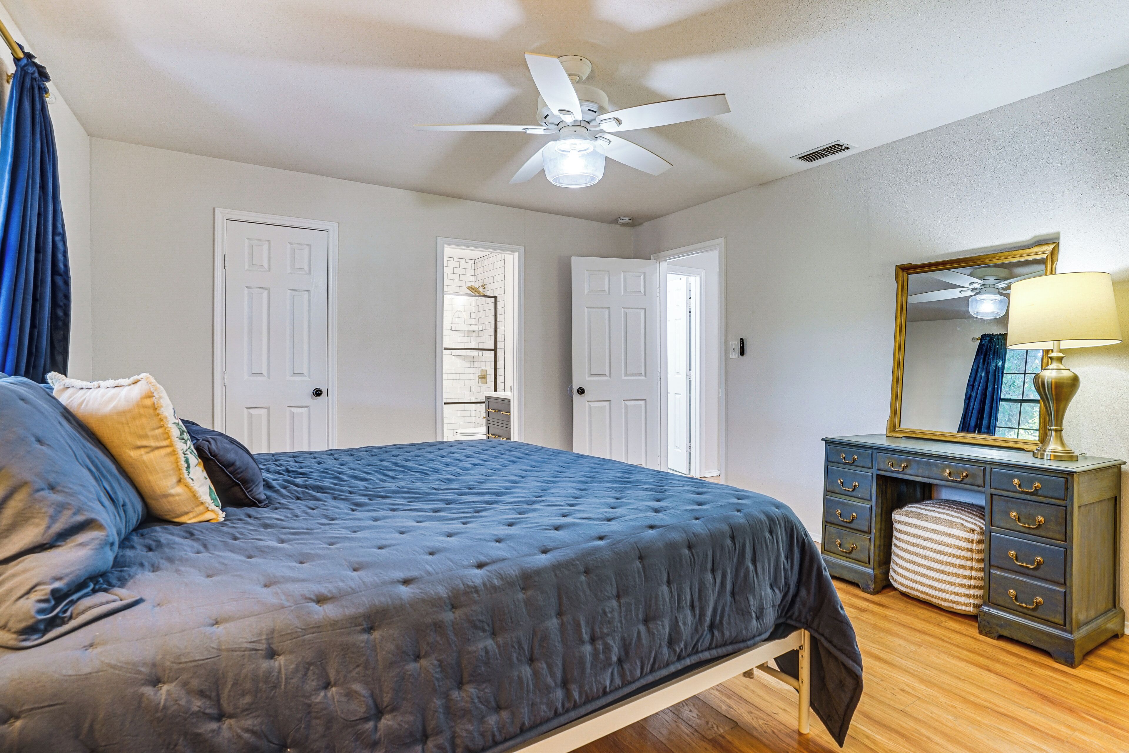 A bedroom with a bed, a dresser, a mirror, and a ceiling fan.