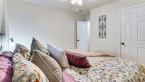 A bedroom with a bed, pillows, a ceiling fan, a door, and a wall decoration.