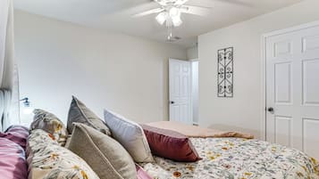 Een slaapkamer met een bed, kussens, een plafondventilator, een deur en een decoratie aan de muur.