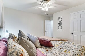 Une chambre à coucher avec un lit, des oreillers, un ventilateur de plafond, une porte et un élément décoratif mural.
