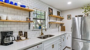 A modern kitchen with white cabinets, stainless steel appliances, and a window with a view of trees.