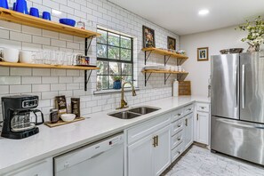 Une cuisine moderne avec des meubles blancs, des appareils en acier inoxydable et une fenêtre donnant sur les arbres.