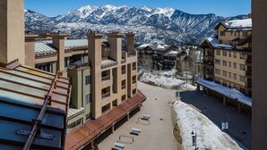 A hotel with multiple floors, a covered outdoor area with benches, and a view of snow-covered mountains in the background.